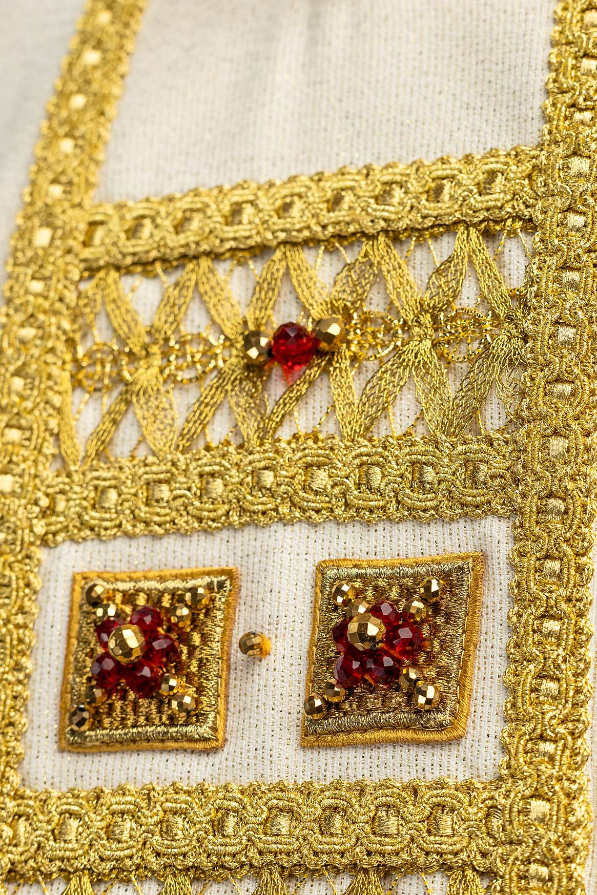 Chasuble, gros plan sur la broderie dorée ajourée et les pierres rouges