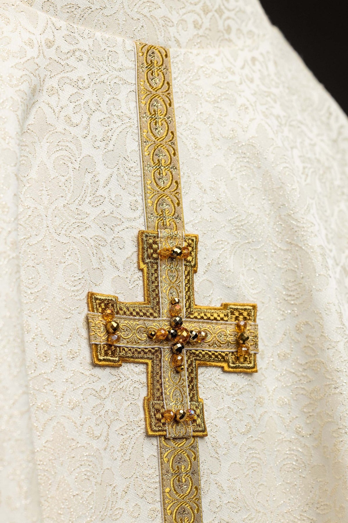 Chasuble ivoire, gros plan sur la croix dorée ornée de pierres naturelles